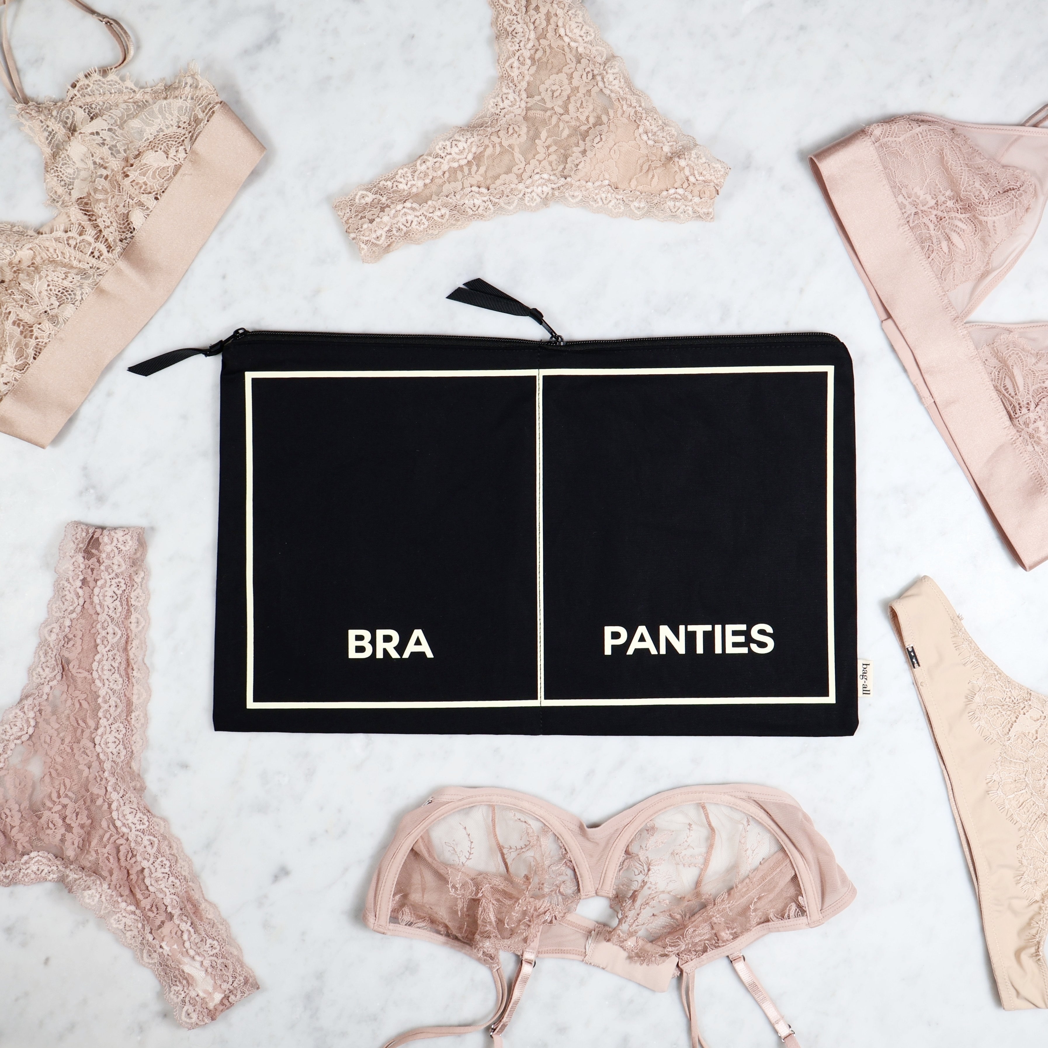 Bag-all black lingerie pouch labeled bra and panties surrounded by lace underwear on marble surface