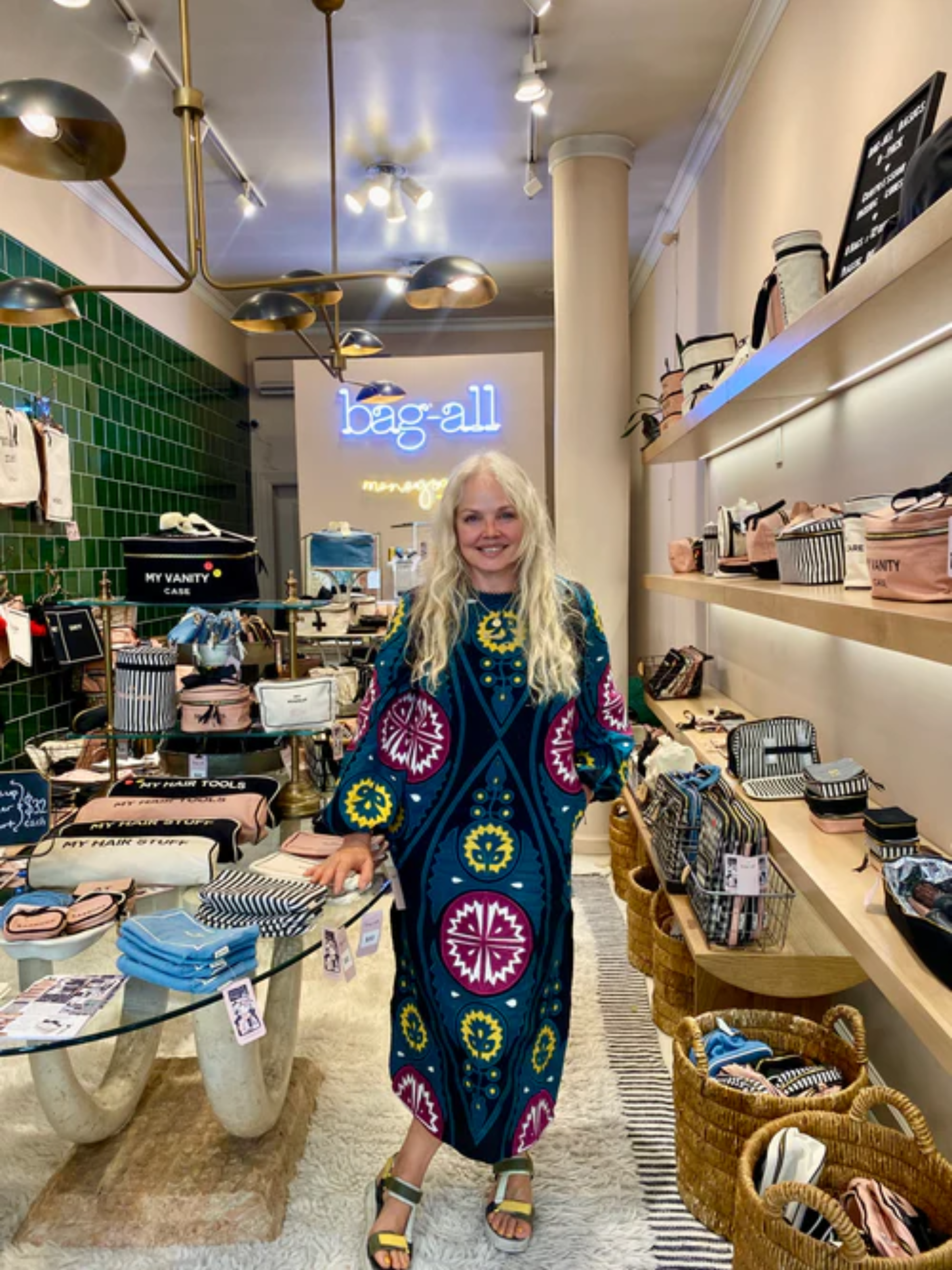 Woman in patterned dress smiling inside Bag-all store surrounded by organizing bags and woven baskets gallery position 1