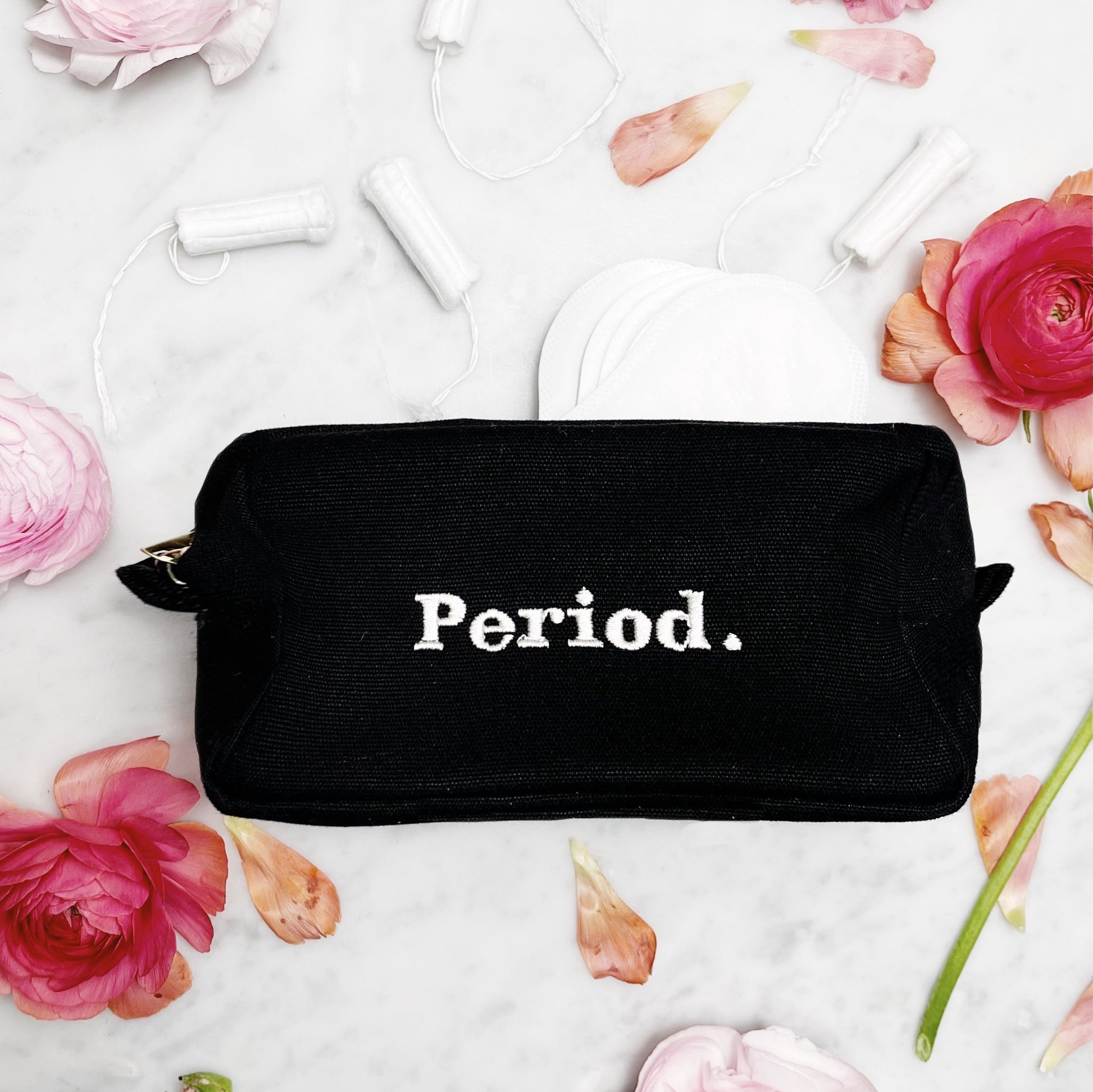 Bag-all Stylish Sanitary Pouch in black canvas with white Period embroidery, surrounded by pink roses and feminine essentials on white background