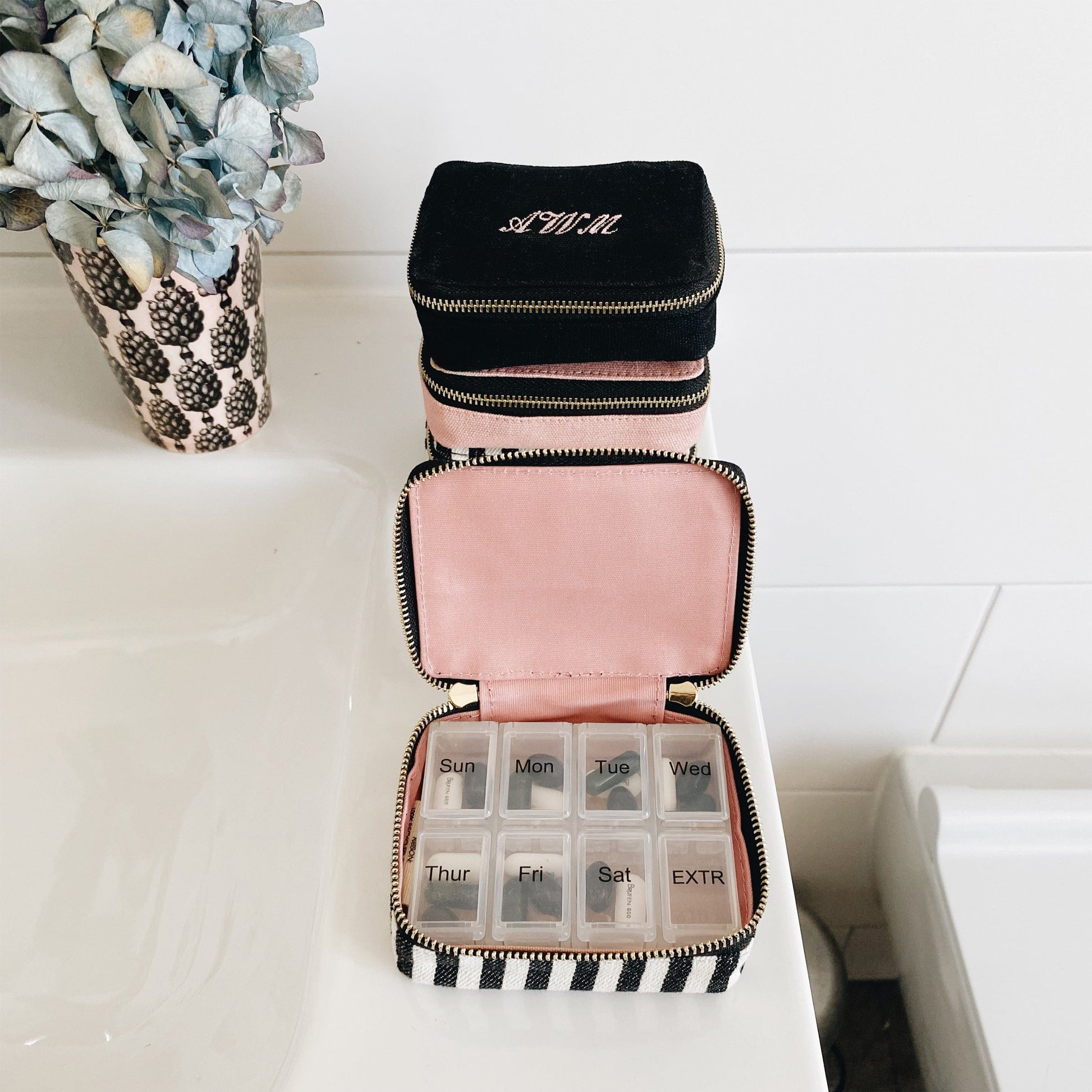 Bag-all Pill Organizing Case with Weekly Pill Organizer featuring black exterior, pink interior, striped pattern, and 8-compartment weekly organizer. Monogrammable cotton case with secure zipper closure.