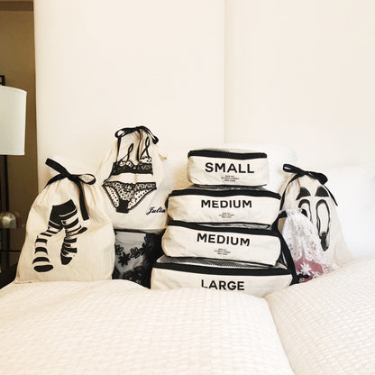 Bag-all Sock Short Bag in Cream - Organized storage solution featuring stackable cotton bags with size labels and black ribbon ties, displayed on white bedding alongside lingerie and sock bags