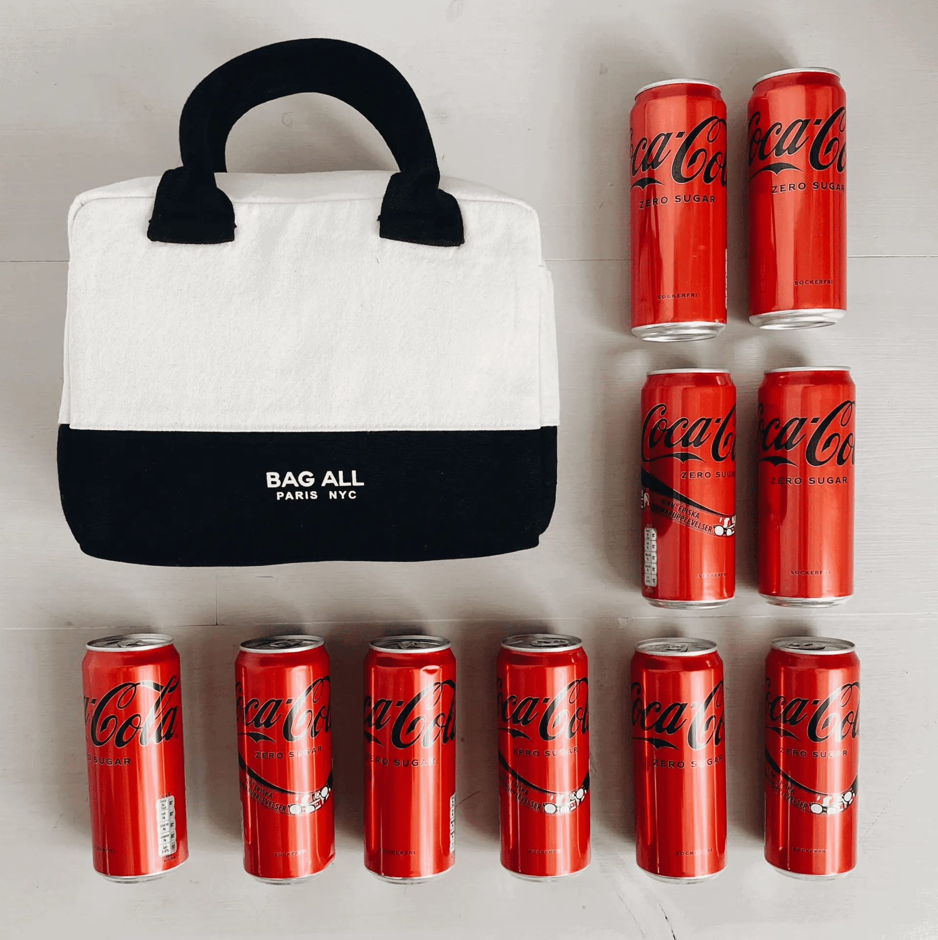 Bag-all Stylish Monogram Lunch Box in cream and black cotton canvas shown with Coca-Cola cans for size reference, featuring padded handles and insulated interior