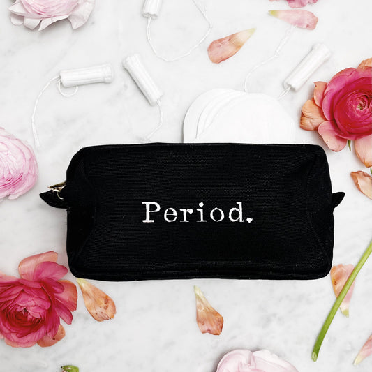 Black Bag-all pouch with white "Period." text surrounded by tampons and pink flowers on marble surface