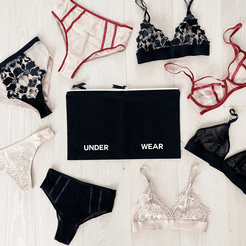 Bag-all Double Lingerie Packing Pouch in black with UNDER WEAR text, surrounded by matching lingerie sets in black, red, and beige, displayed on white wooden surface