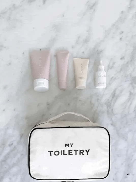 Bag-all cream toiletry organizer bag with black trim and handle labeled My Toiletry on marble background with skincare bottles