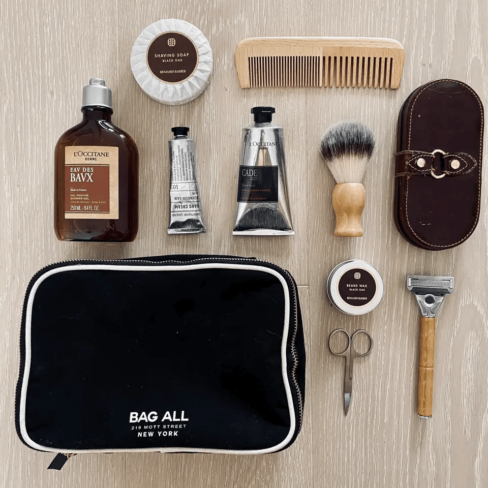 Bag-all Double Sided Toiletry Case in Black shown with grooming essentials including shaving brush, comb, lotions, and travel-sized toiletries on wooden surface, featuring waterproof lining and dual zipper design