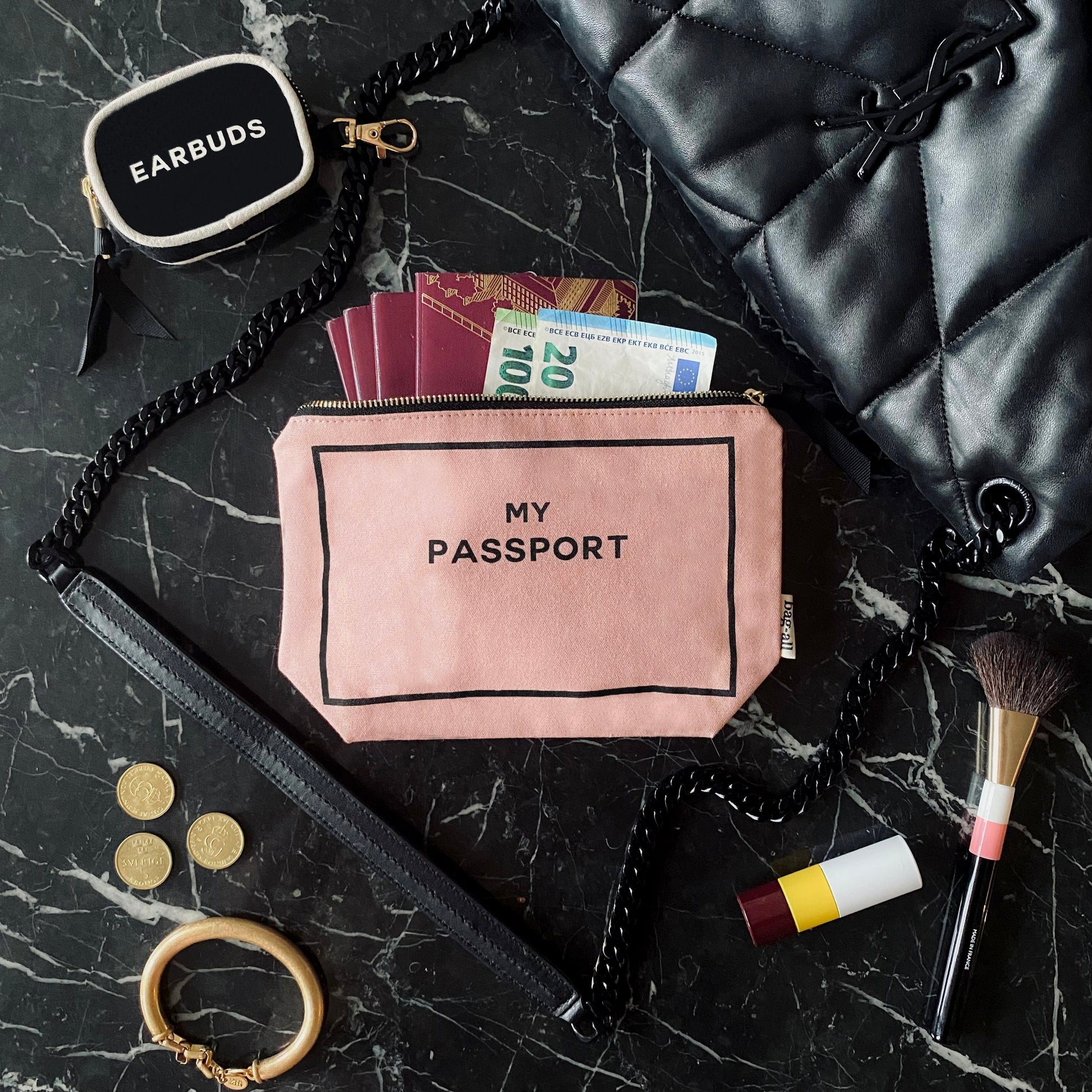 Bag-all pink passport organizer with cash and documents on marble surface with makeup and accessories nearby