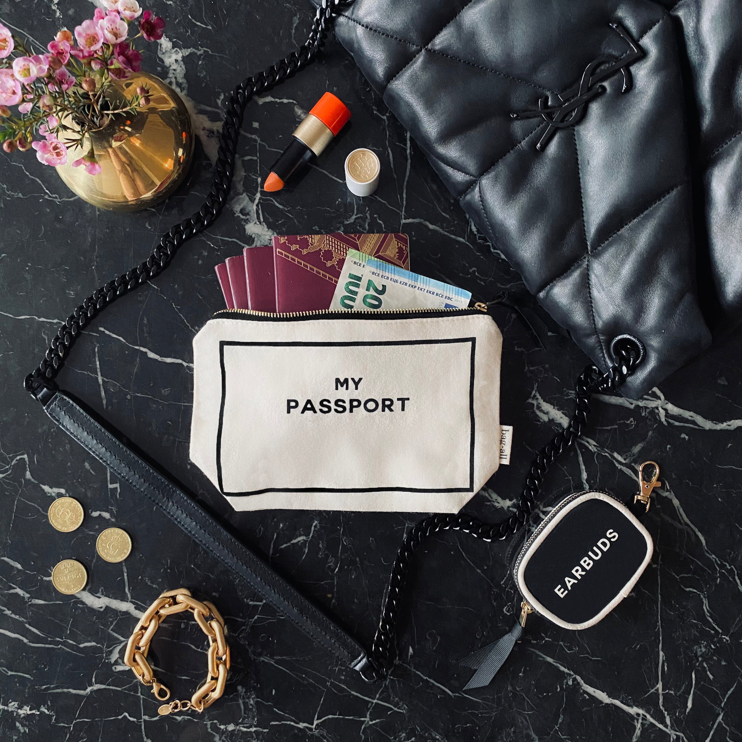 Bag-all cream passport organizer pouch with travel essentials on black marble surface with black leather bag and accessories