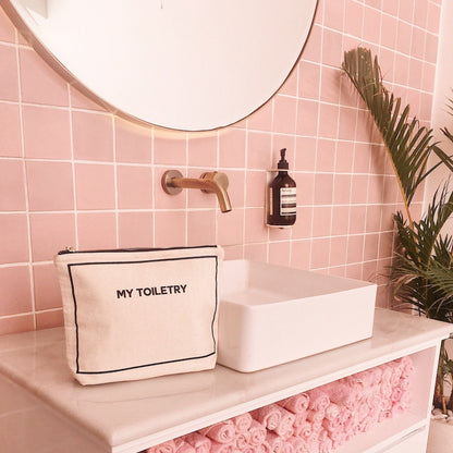 Bag-all Toiletry Travel Gift Set 4-Pack Cream featuring My Toiletry pouch in natural cotton displayed on modern pink bathroom counter with brass faucet and decorative palm leaf