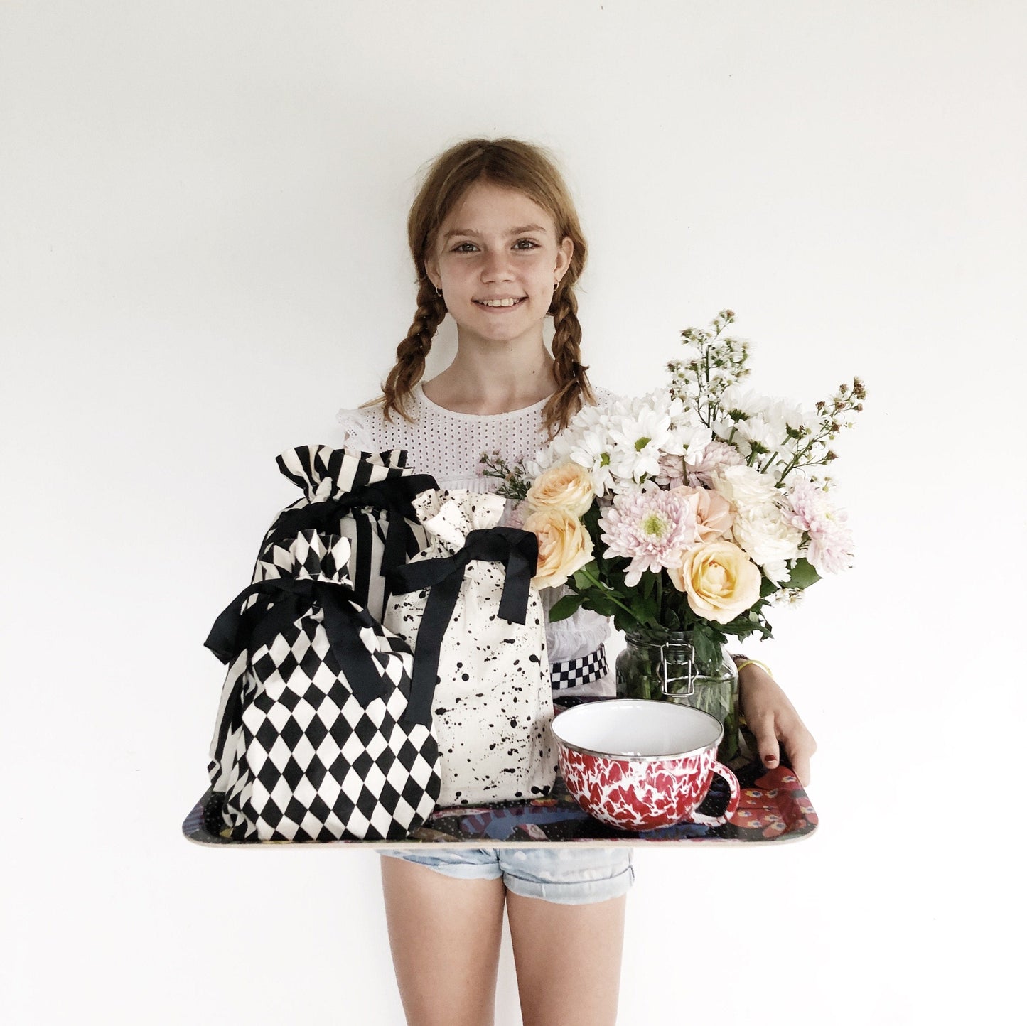 A girl holding a tray with coffee, flowers and many reusable gift bags holding multiple gifts. 