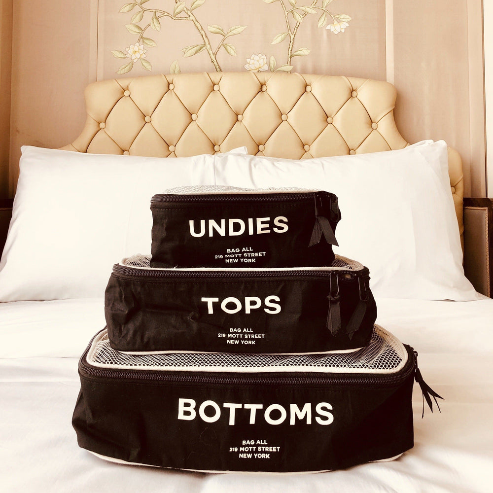 A bed with three black packing cubes labeled small, medium and large. 