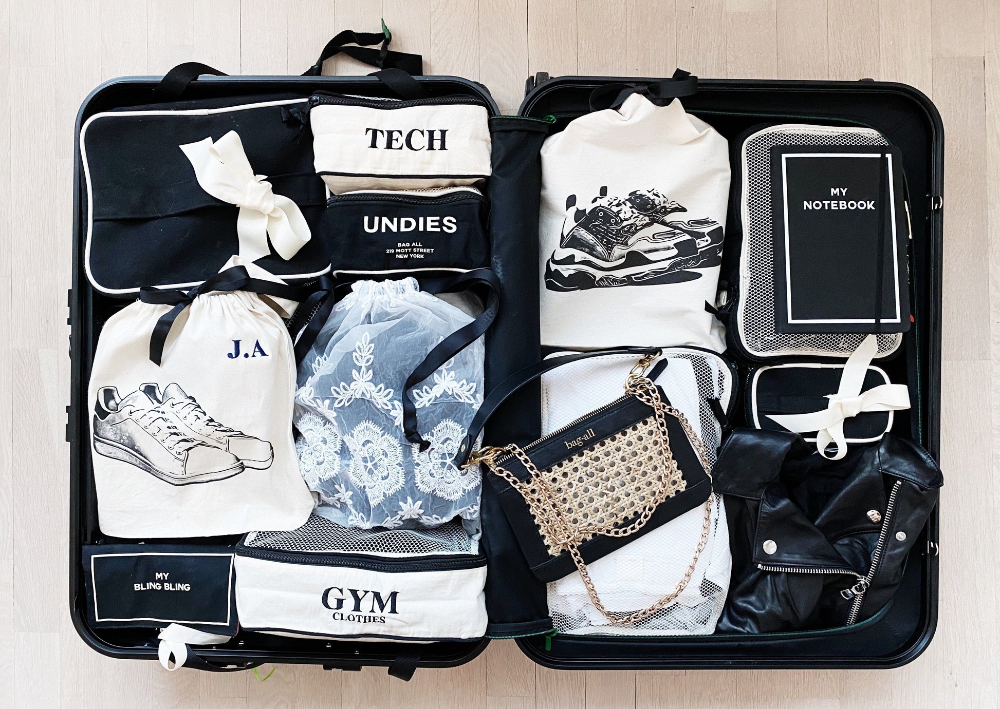Bag-all Cotton Packing Cubes 3-pack Cream - Organized suitcase interior showing labeled storage bags for clothes, tech, gym gear, and accessories in black and white color scheme