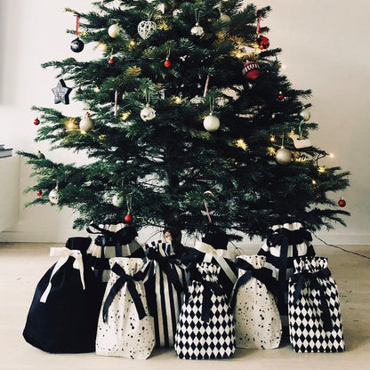 Bag-all Gift Bag Striped Medium displayed under Christmas tree alongside black and white patterned reusable gift bags, showcasing sustainable holiday gift wrapping alternatives with elegant patterns