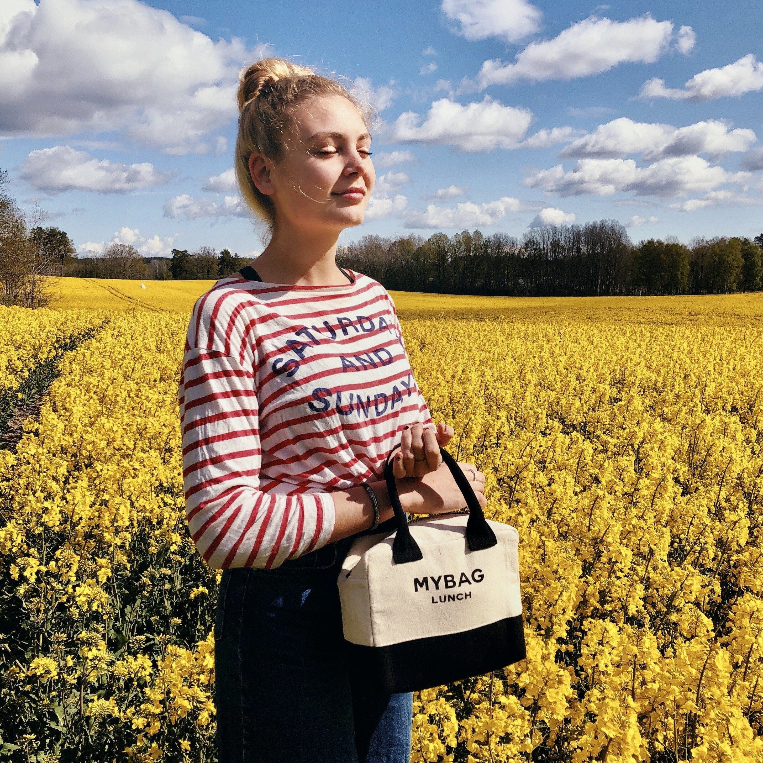 A girl in a flower garden holding her lunch box.