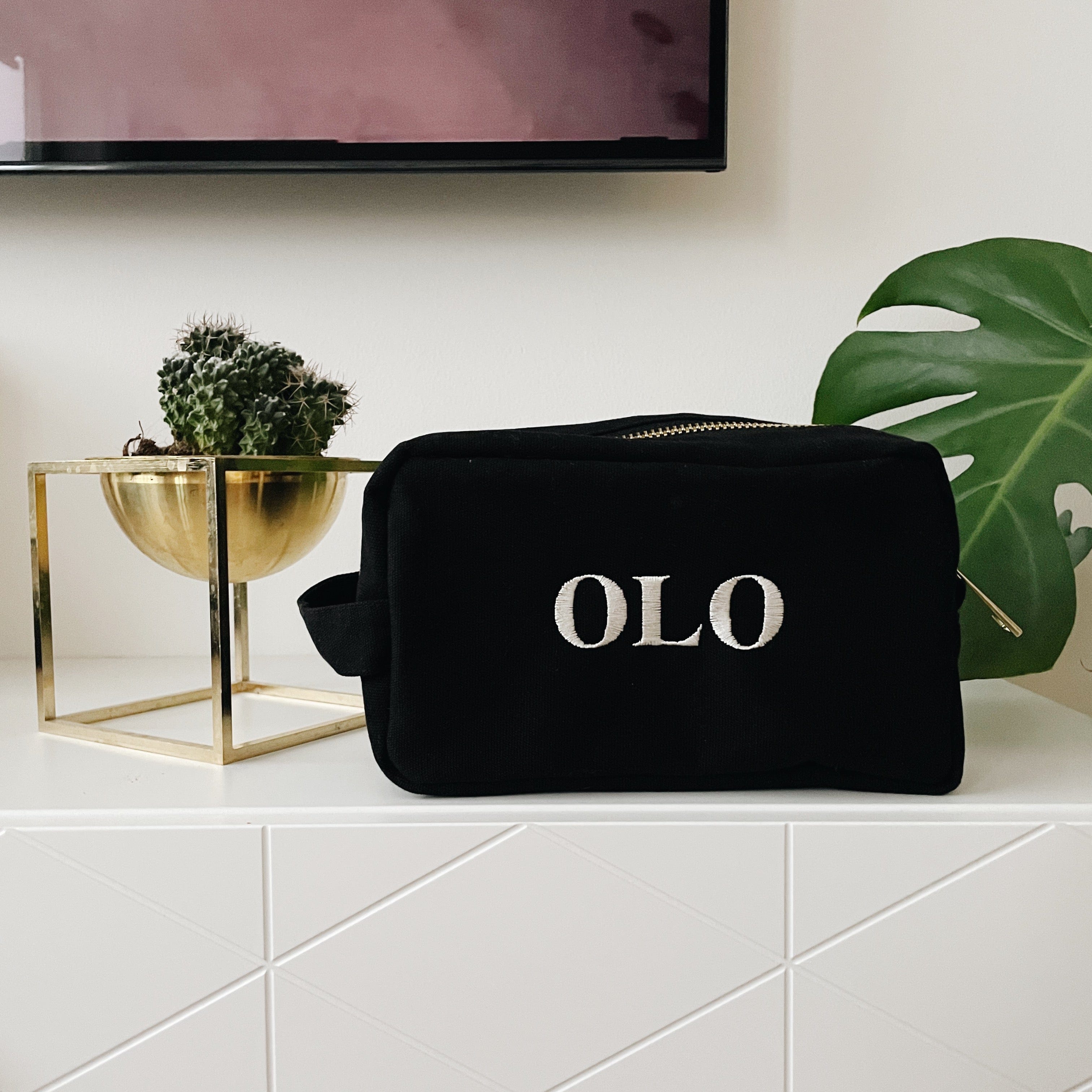 Toiletry souki case surrounded by plants and "OLO" monogrammed on  it. 