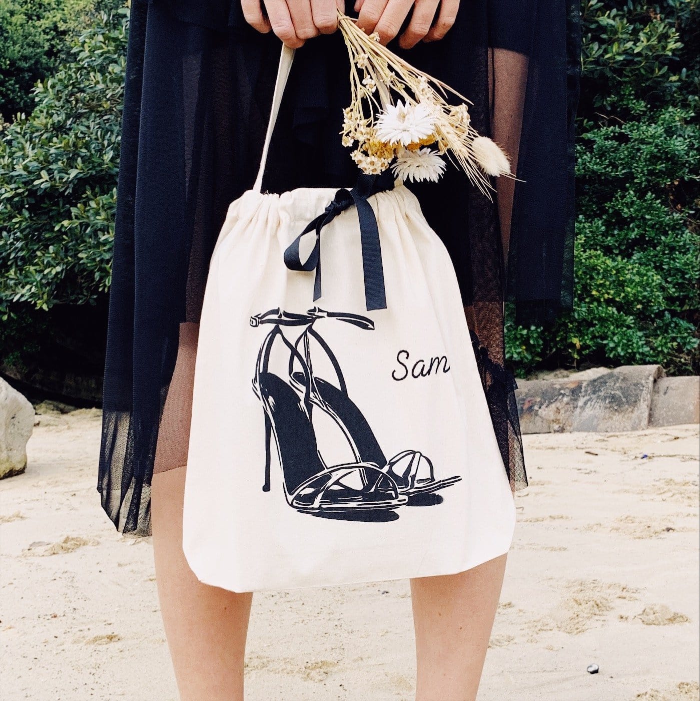 A girl in a black dress holding flowers and high heel sandals.