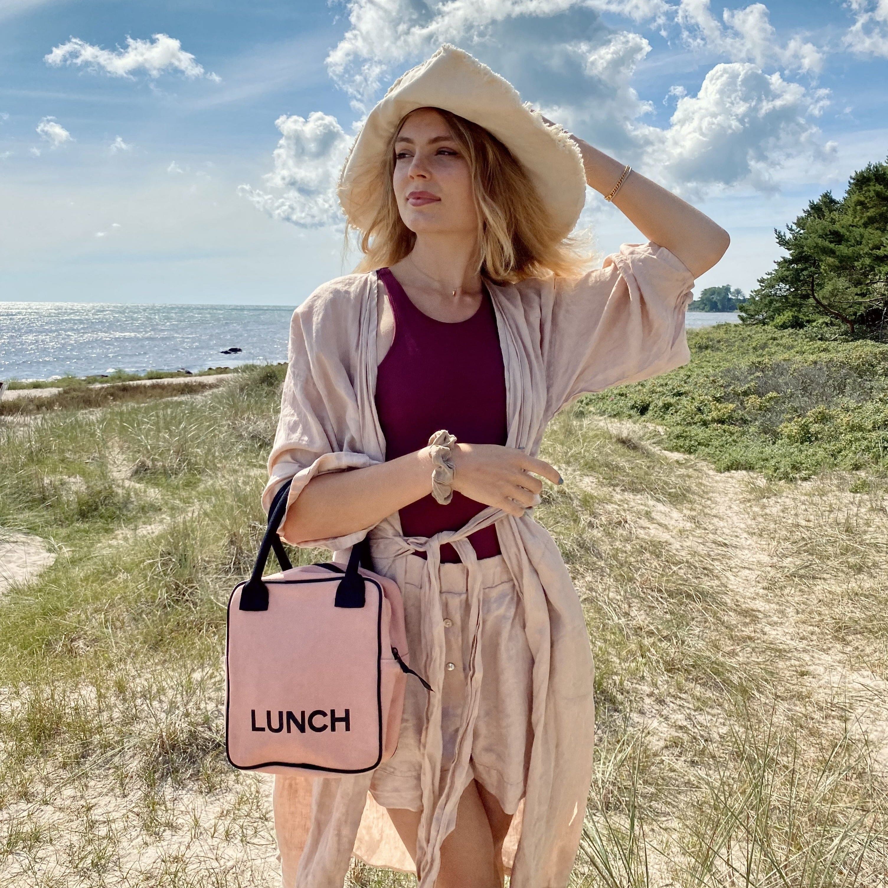 A girl at the beach with her pink lunchbox. 