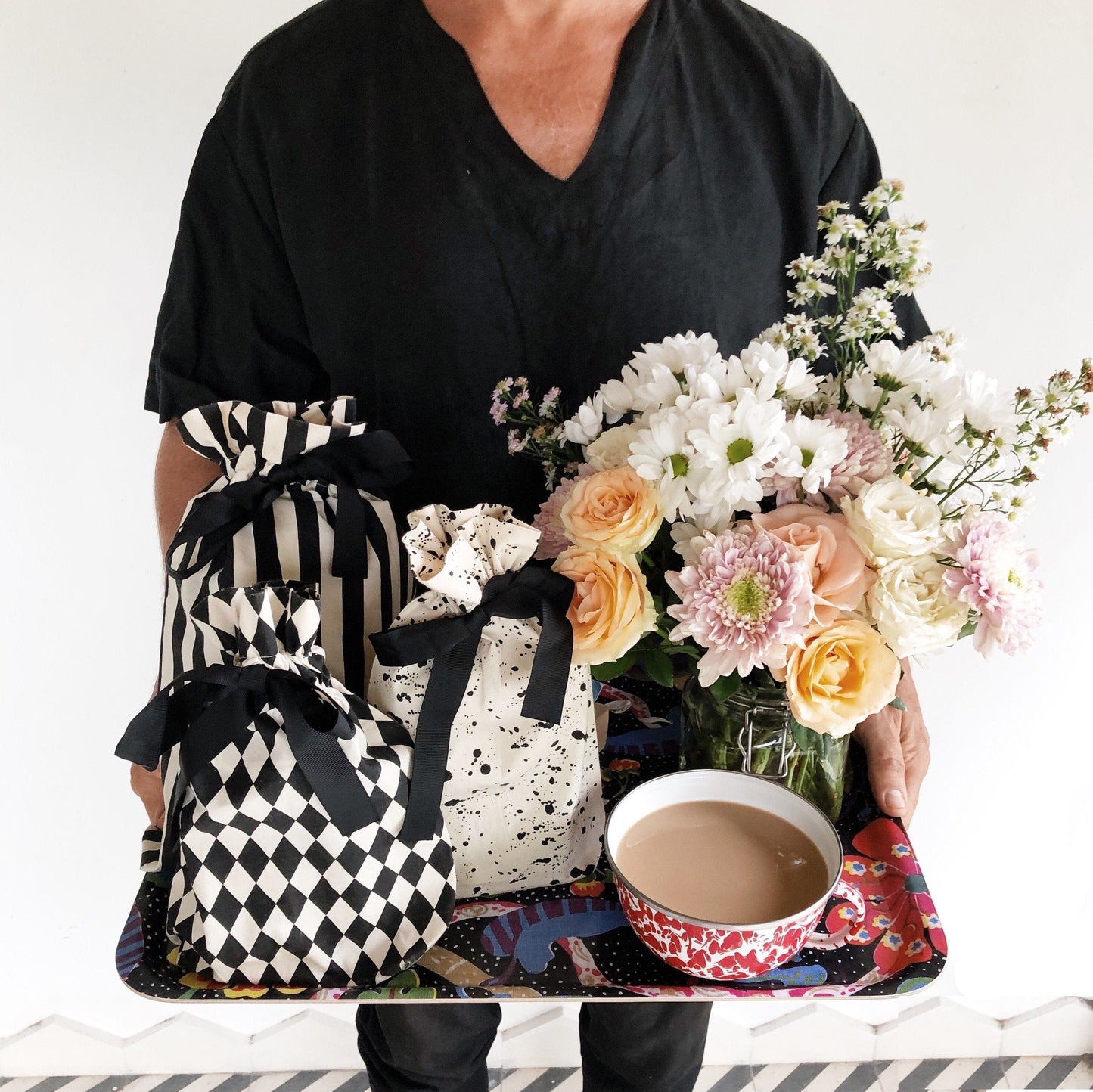 A tray with coffee, flowers and patterned reusable gift bags. 
