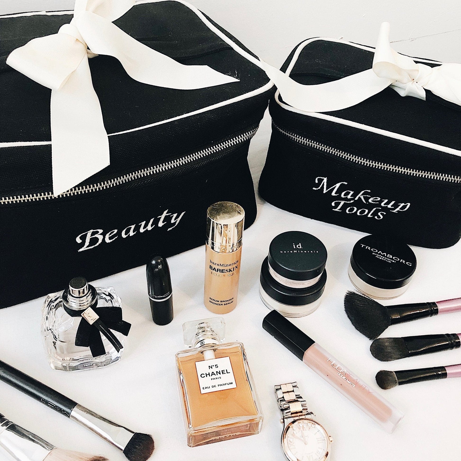 Bag-all monogram beauty case and makeup tools organizer with elegant white bows, displayed with luxury cosmetics, perfumes, and brushes in classic black and white design