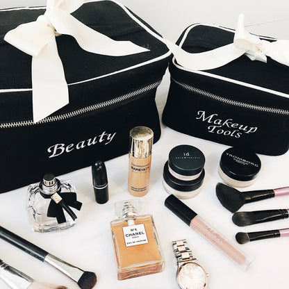 Bag-all monogram beauty case and makeup tools organizer with elegant white bows, displayed with luxury cosmetics, perfumes, and brushes in classic black and white design