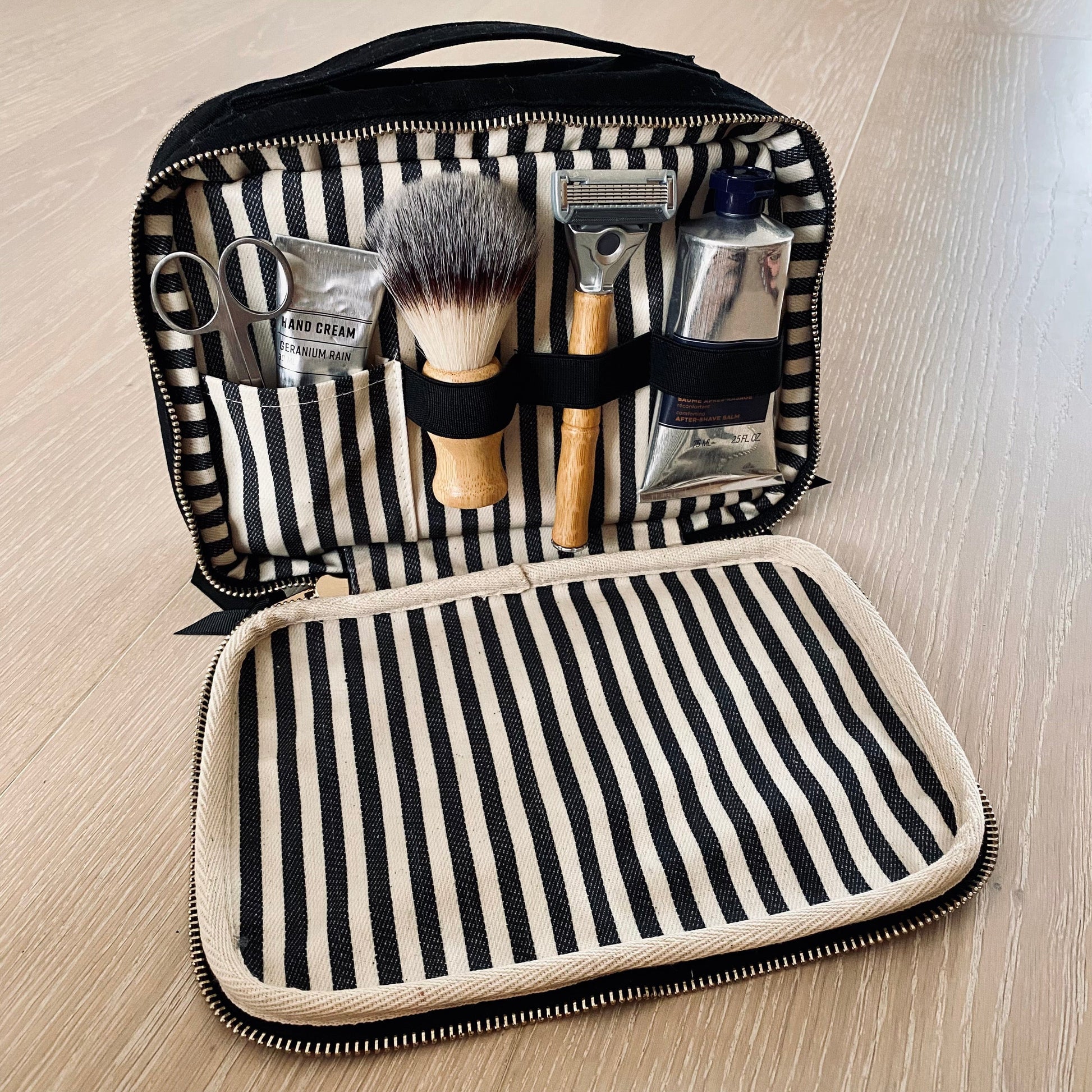 Bag-all Double Sided Toiletry Case in Black featuring striped interior, elastic bands holding grooming tools, waterproof lining, dual zippered compartments, and carrying handle