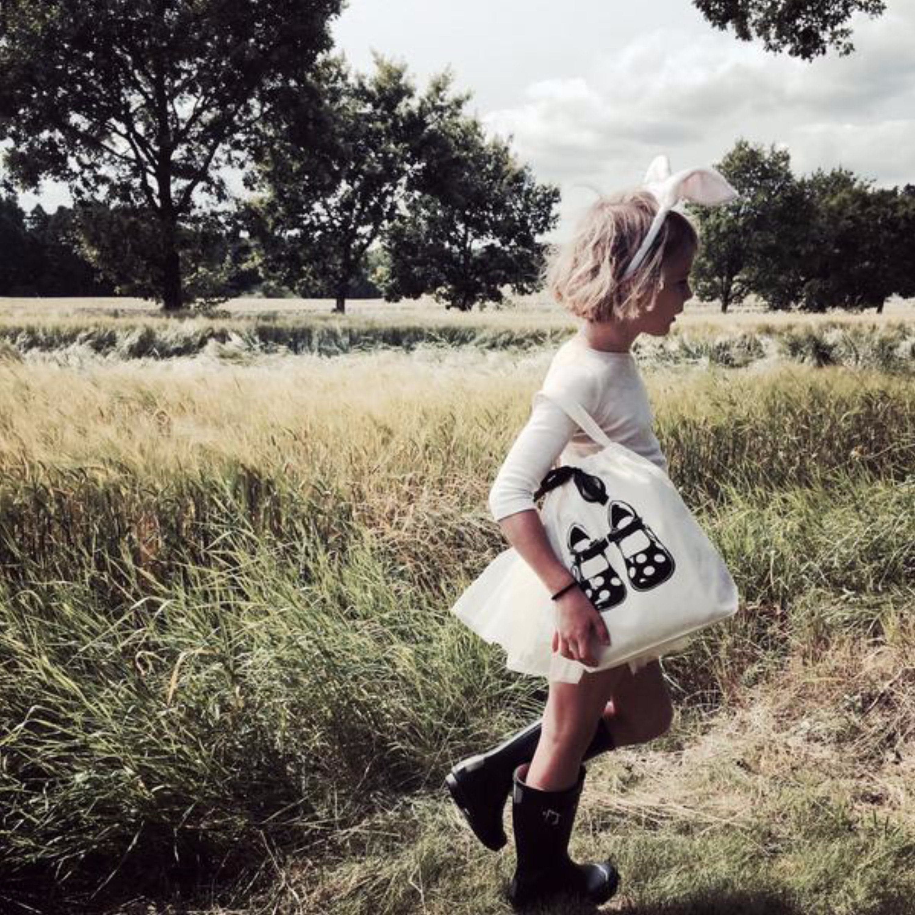 A child in a grassy field with a shoe bag. 